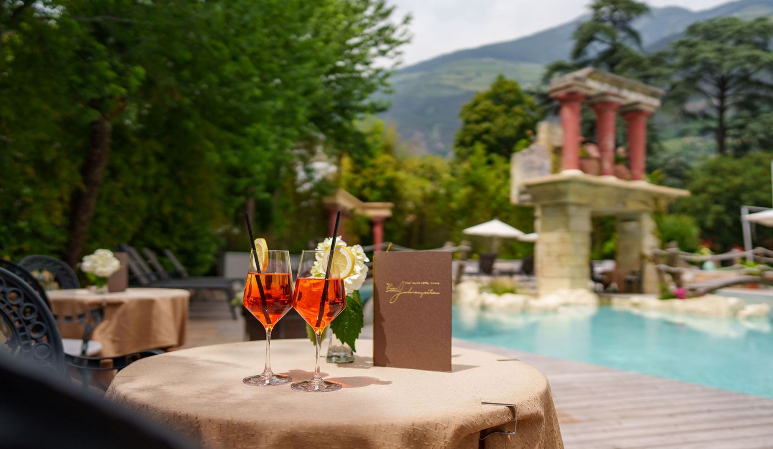 Hotel Vier Jahreszeiten Schlanders Terrasse mit Garten und Café bei sonnigem Wetter Hotel Vier Jahreszeiten Schlanders Terrasse mit Garten und Café bei sonnigem Wetter